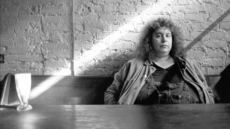 Black-and-white image of woman with curly hair sitting behind a table