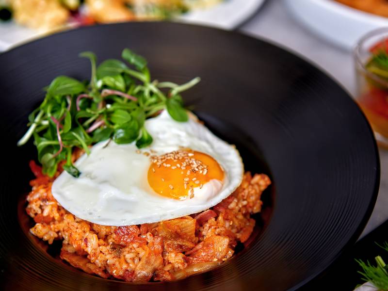 Fried kimchi on a black plate, topped with a fried egg and garnished with watercress.