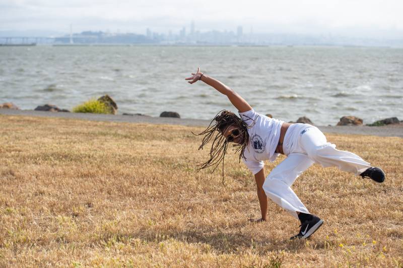 A woman is practicing a capoeira move similar to breakdancing on a golden field in front of the bay in Berkeley, CA