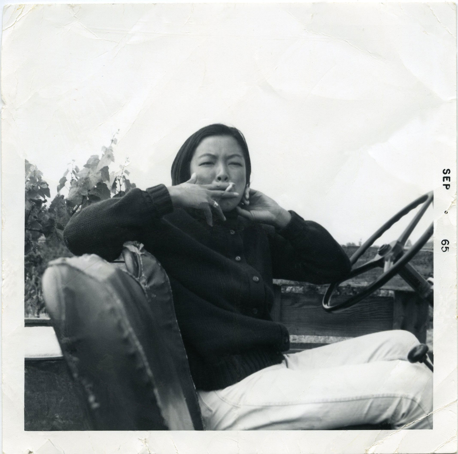 Black and white image of an Asian American woman smoking a cigarette in a car