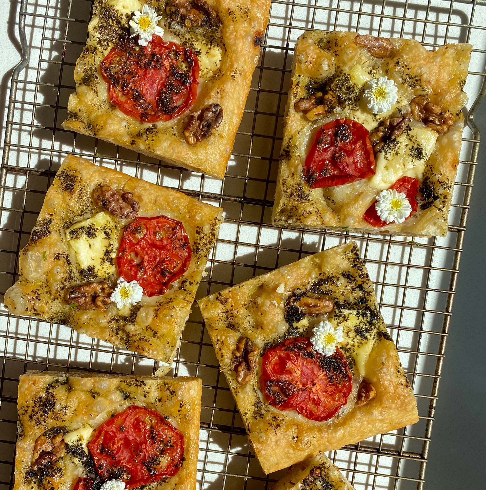 Squares of tomato and herb-topped focaccia on a cooling rack.