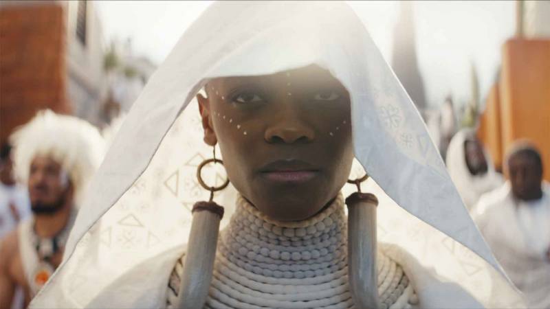 A black woman in a white thin headpiece and decorative earrings, backlit by the sun