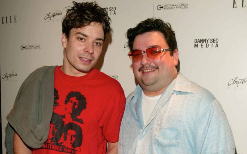 Jimmy Fallon with tousled hair, wearing a red T-shirt. Next to him is Horatio Sanz wearing sunglasses with red lenses and a blue shirt.