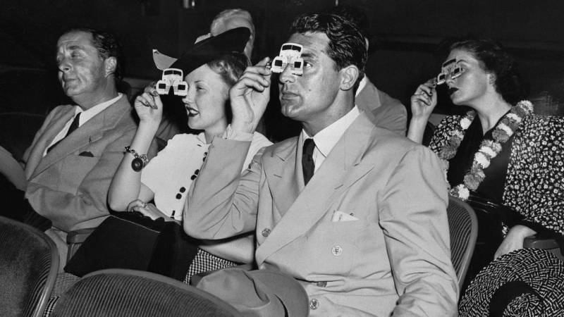Black-and-white image of four people in theater seats with special viewfinders over eyes