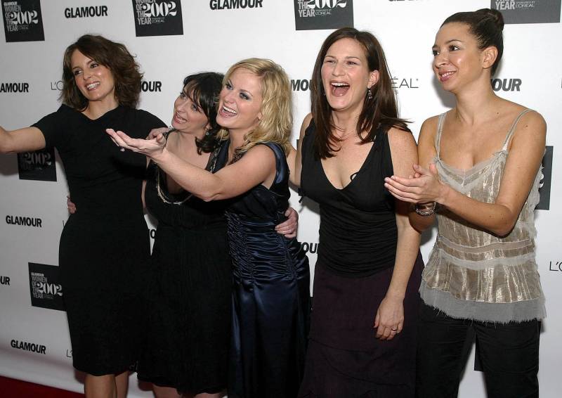A group of five laughing women gesture and goof around on the red carpet.