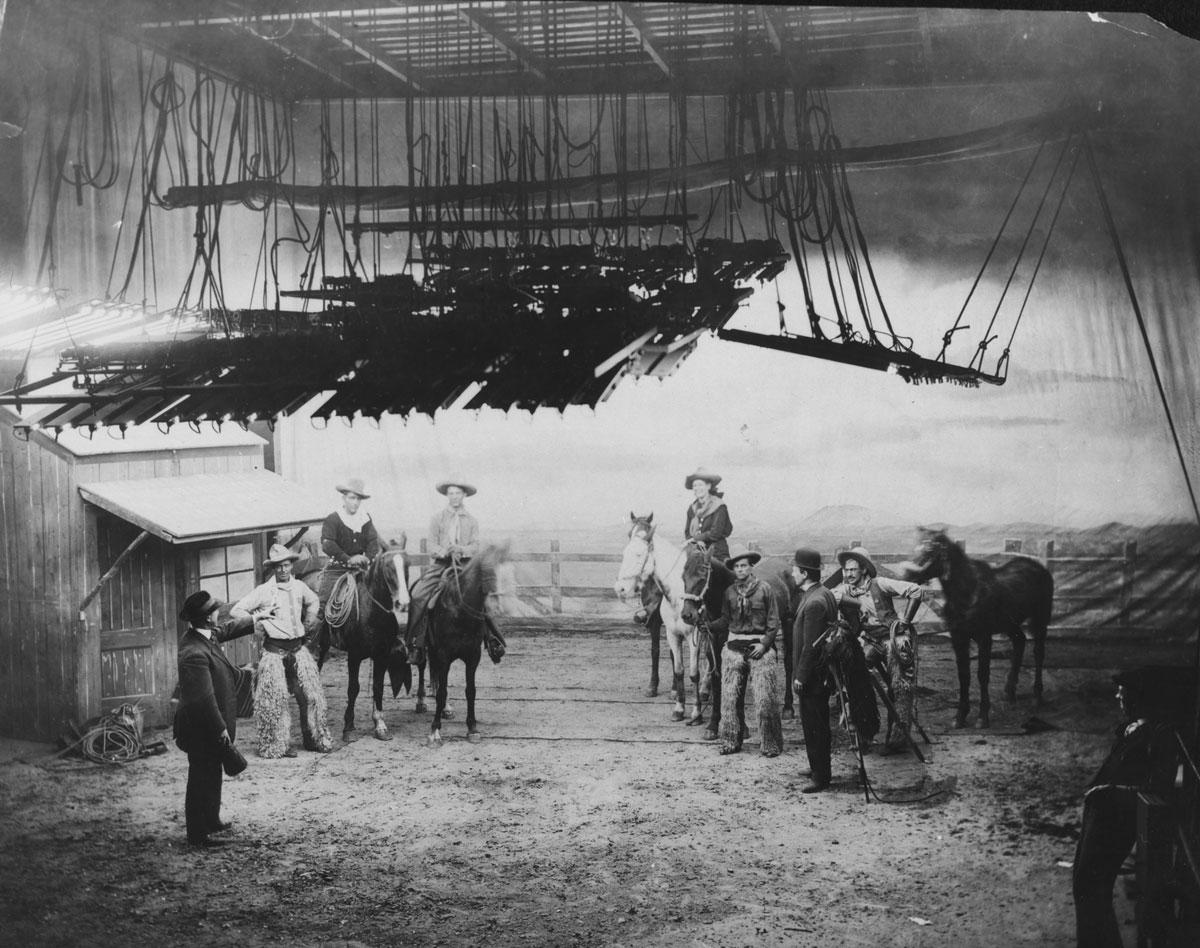 Black-and-white image of movie set, men on horses and lights above