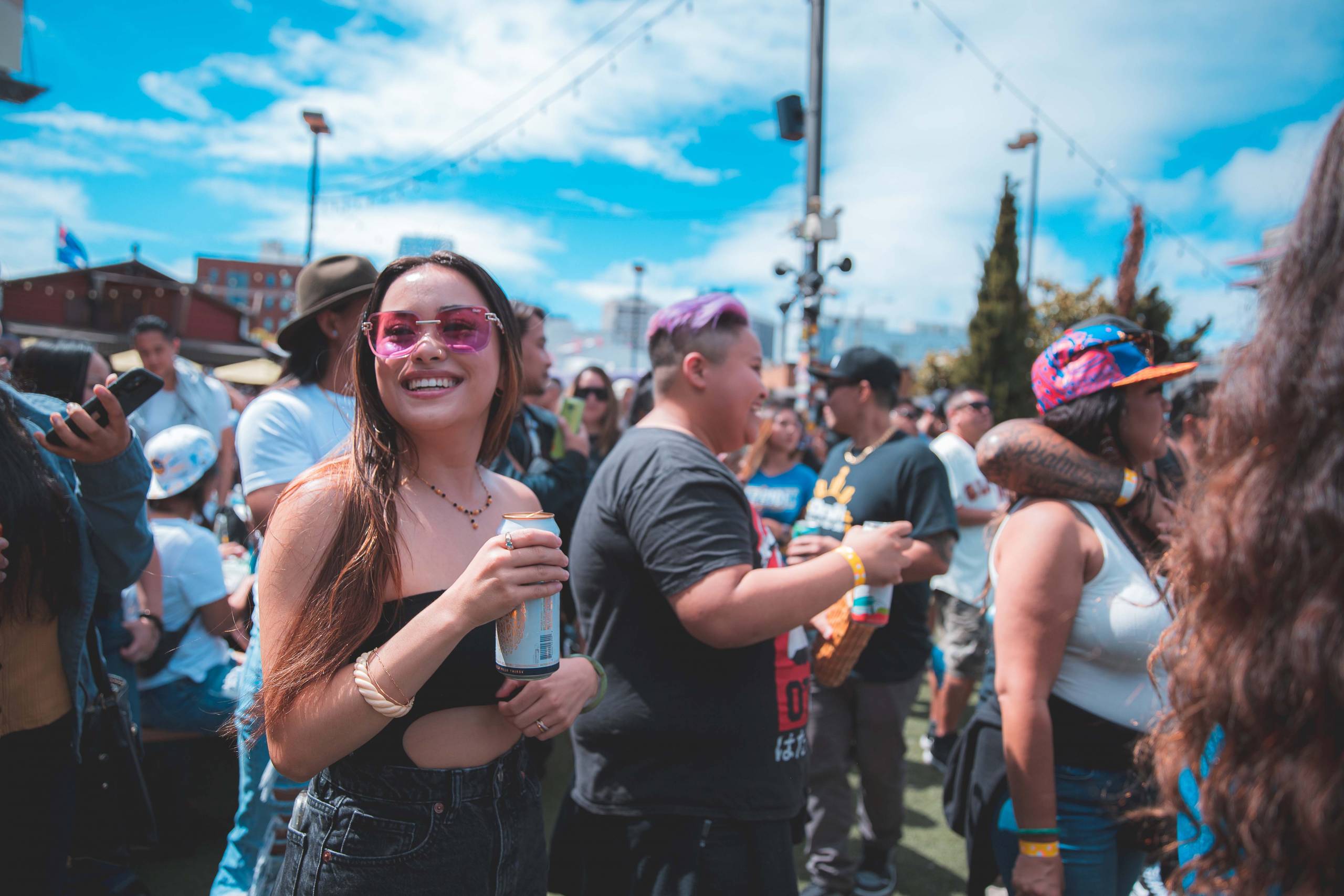 A crowd of festival attendees, many of them holding beer cans, on a beautiful sunny day.