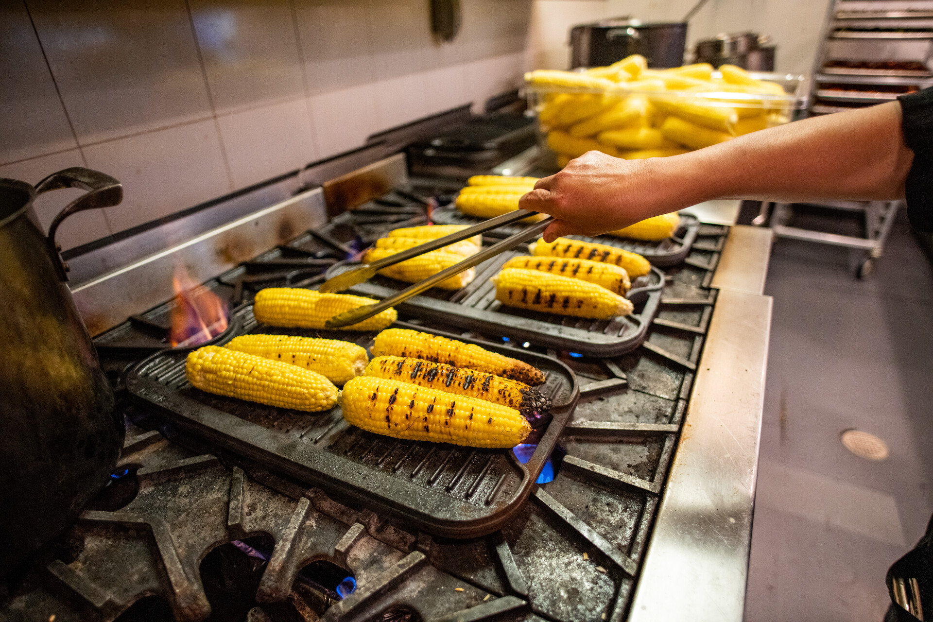 corn is being roasted on a stovetop by an apprentice in the kitchen of Reffetorio