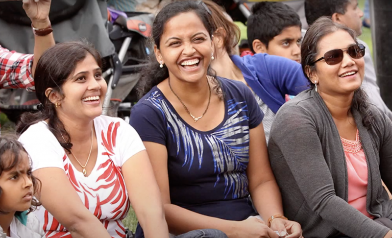 Three South Asian women sitting in a row laughing.