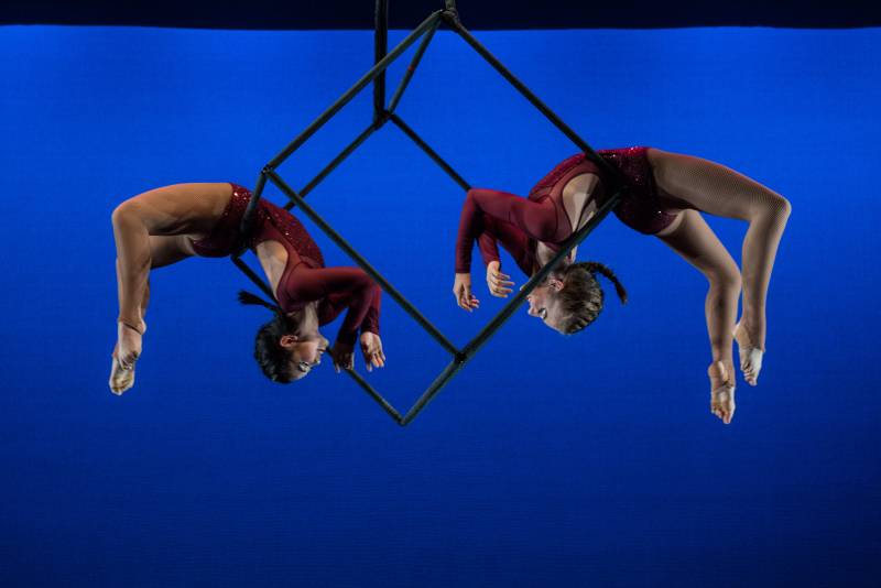 Two aerial artists are suspended on a cage