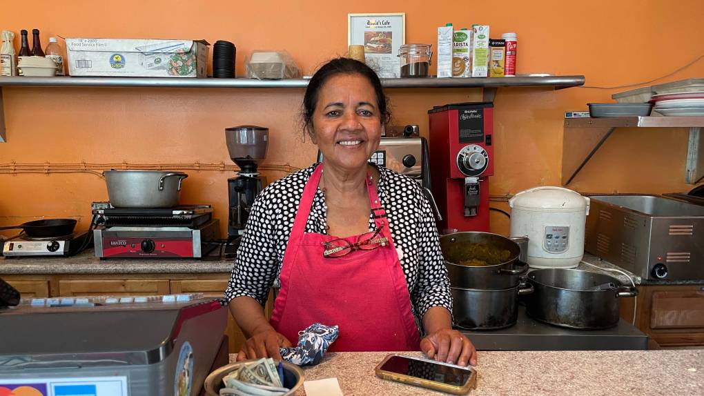 Anula Edirisinghe, in a red apron, poses behind the counter of her restaurant Anula's Cafe.