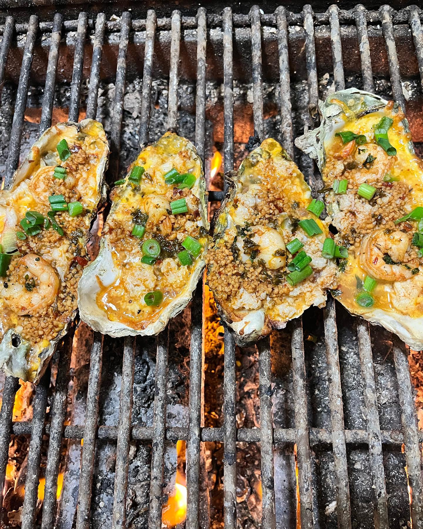 Four oysters, elaborately topped with shrimp, cheese and spices, on a grill.