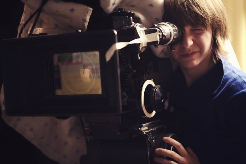 A young woman operating a 35mm film camera. There is a blanket thrown over the camera.