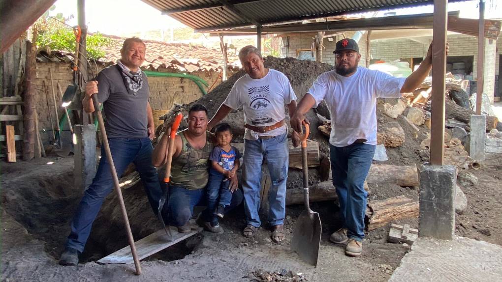 four men and a child are gathered around an outdoor pit, with shovels in hand, where the mezcal is made in Oaxaca, Mexico