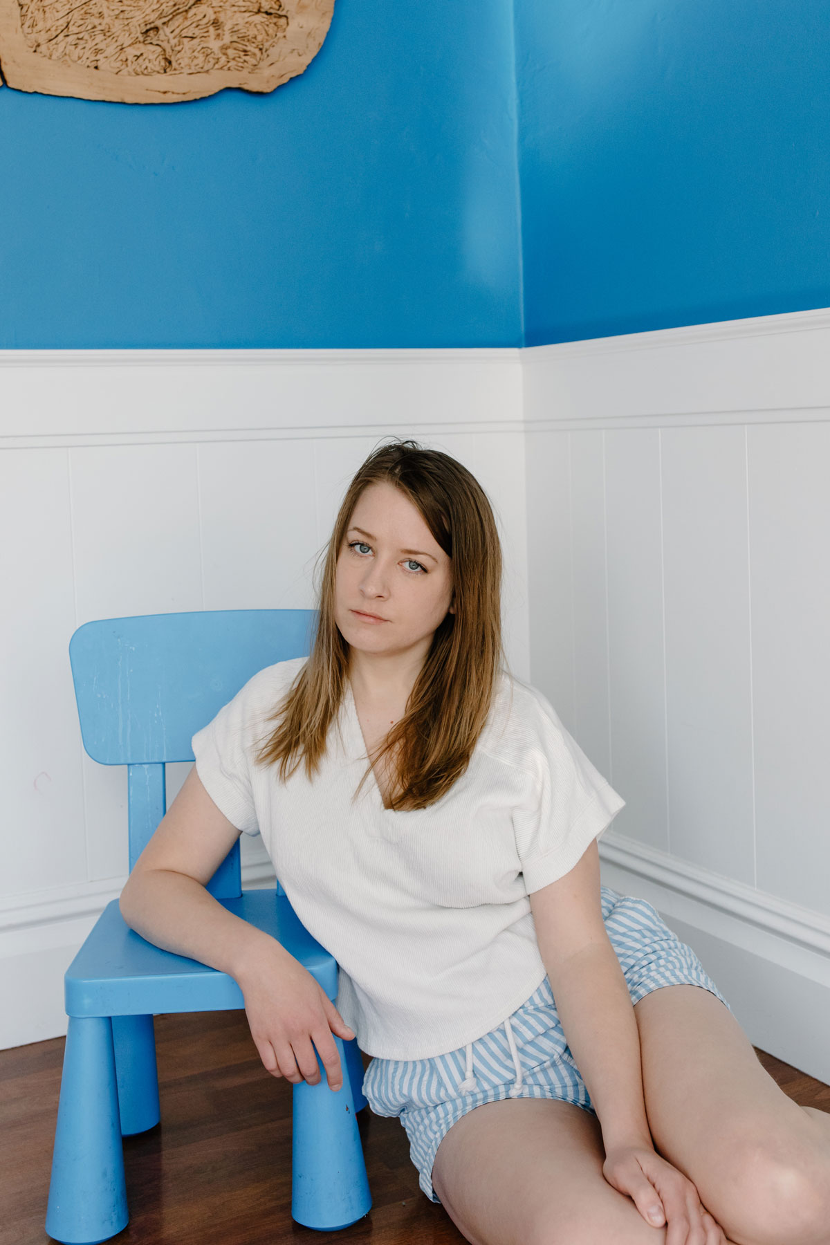 White woman with mid-length brown hair sits on floor in short and T-shirt