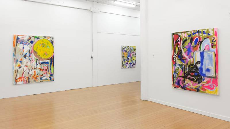 Three large colorful abstract paintings on two white walls