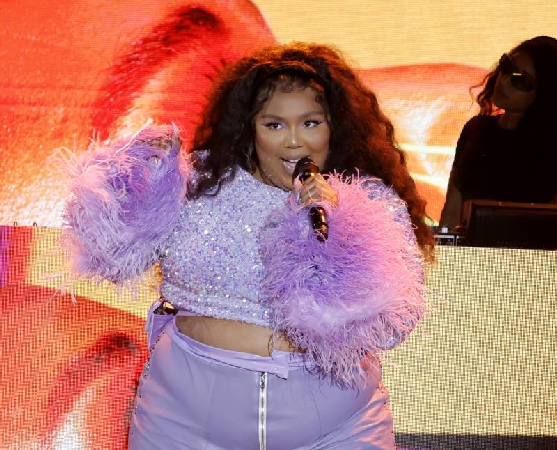 A beautiful plump Black woman wearing flamboyant lilac shorts and dazzling top sings on stage.