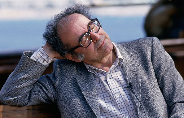 A man in glasses and a suit jacket reclines before the sea.