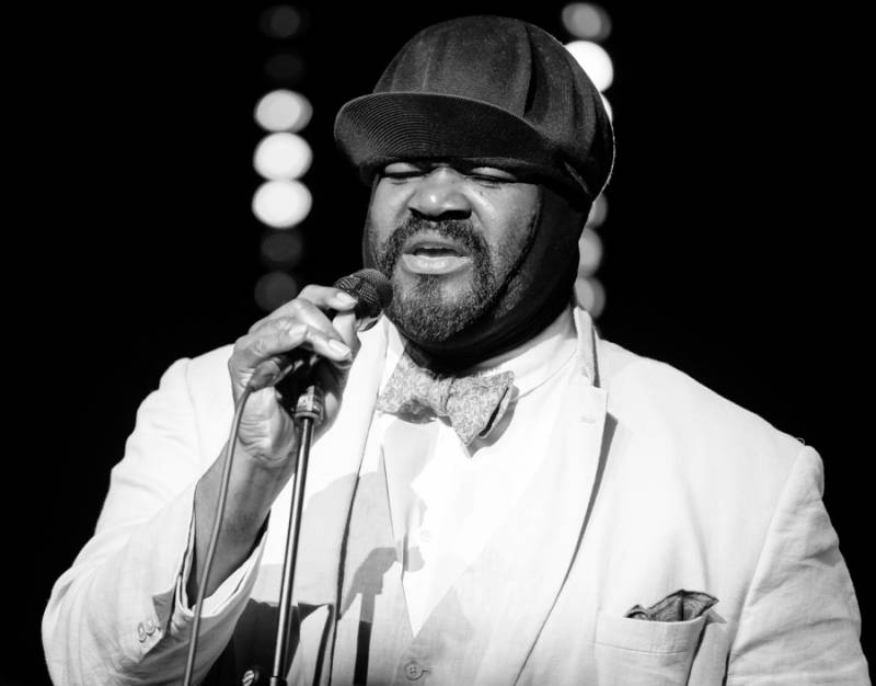 a Black man sings, wearing a white suit and bowtie