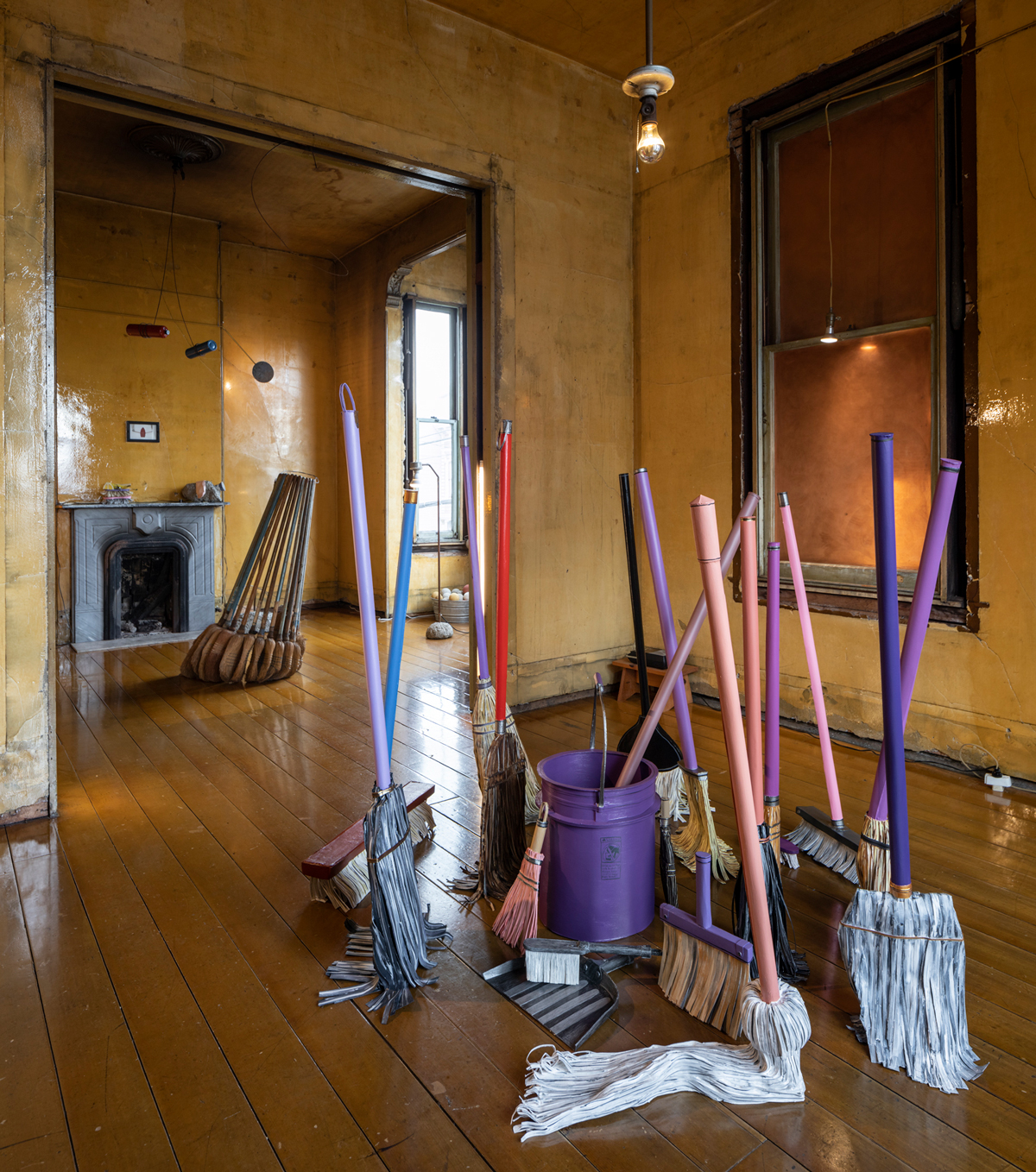 Paper painted brooms stand upright in foreground, leaning broom sculpture in background