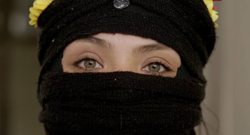 a woman's eyes peer out from a black head/face covering