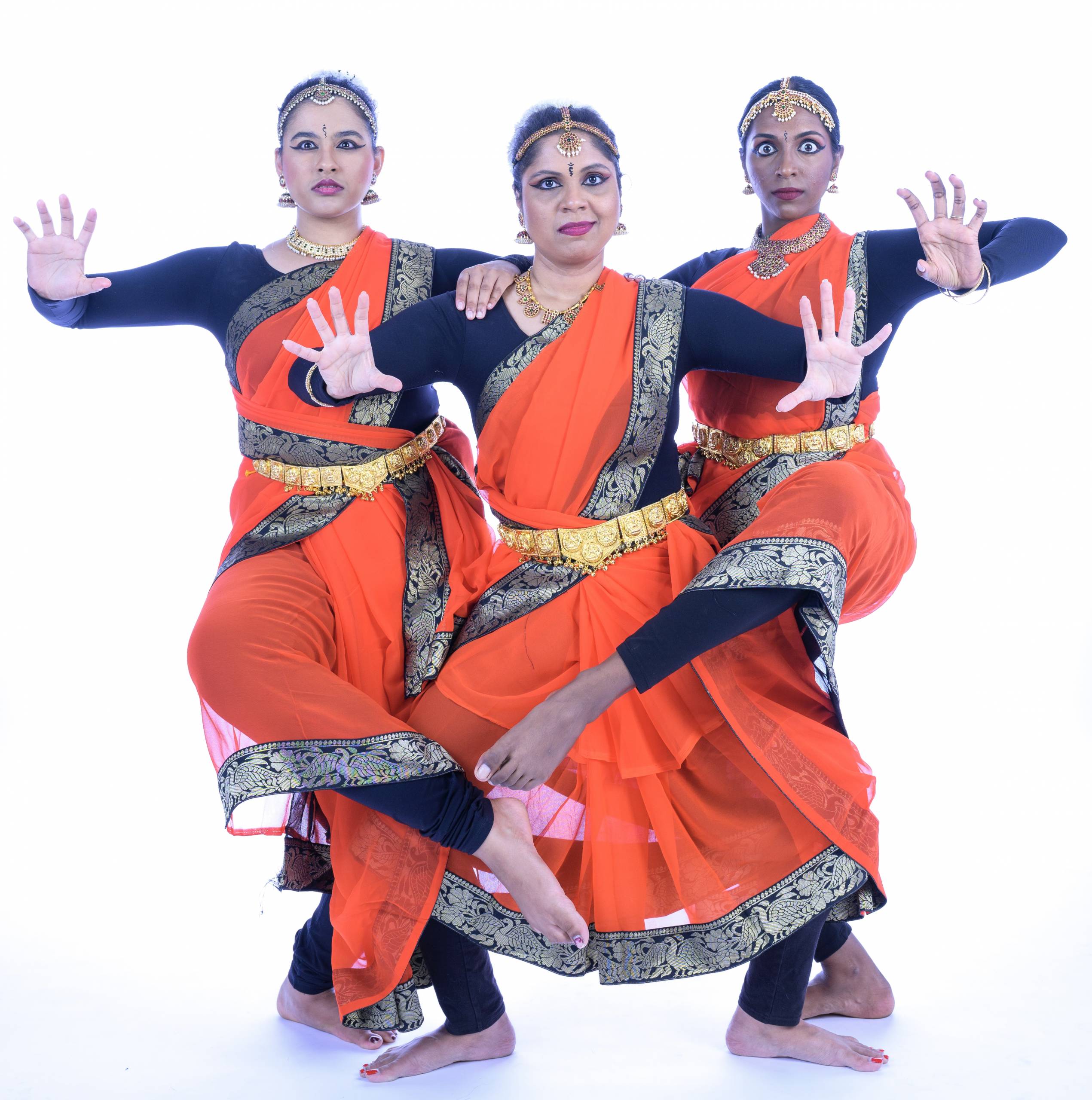 Three Indian dancers in bright orange costumes pose together