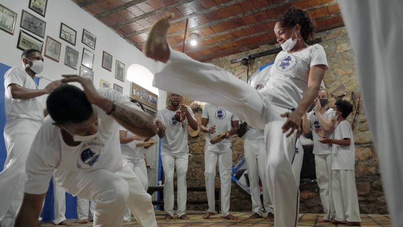 A group of people are playing capoeira in a small room indoors.