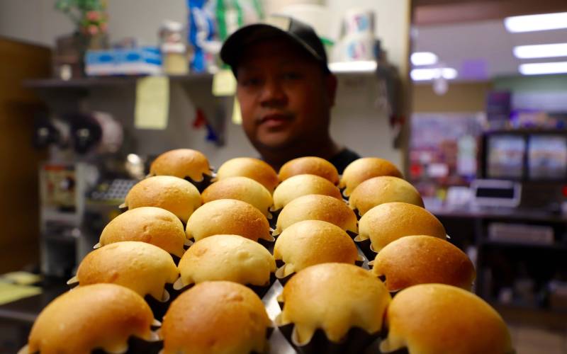 a Filipino foodmaker holds a baking tray of savory rolls known as "pandesal"