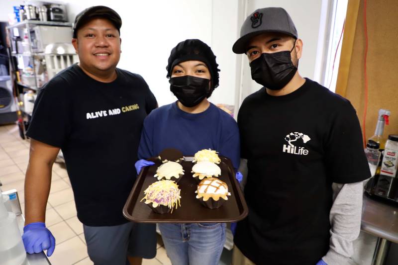 three Ellis Creamery workers display a tray of six ensaymadas, which are Filipino sweet rolls that resemble cupcakes