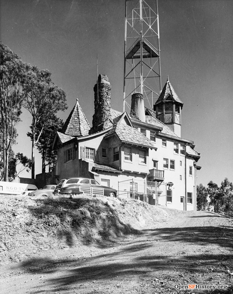 An old mansion with turrets and multiple levels sits incongruously with a giant communications tower emerging from directly behind it.