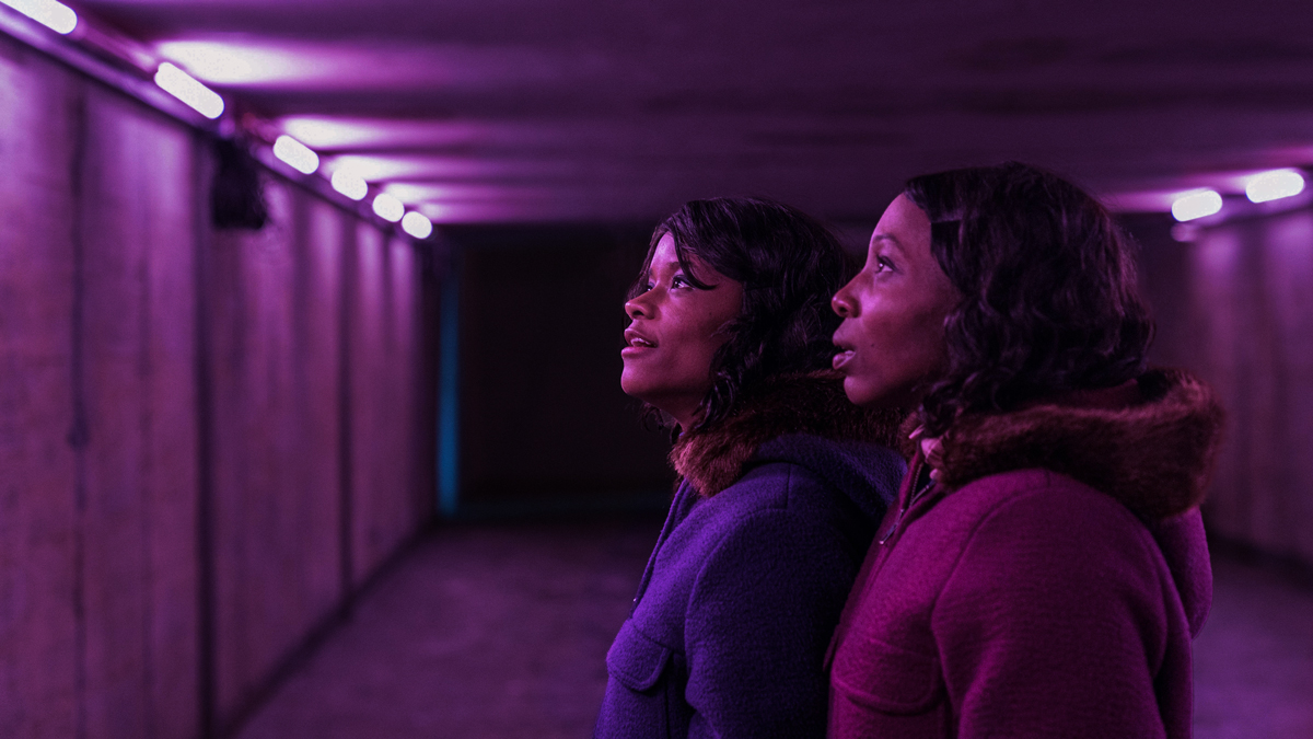 Two young Black women look up in awe at a line of purple lights