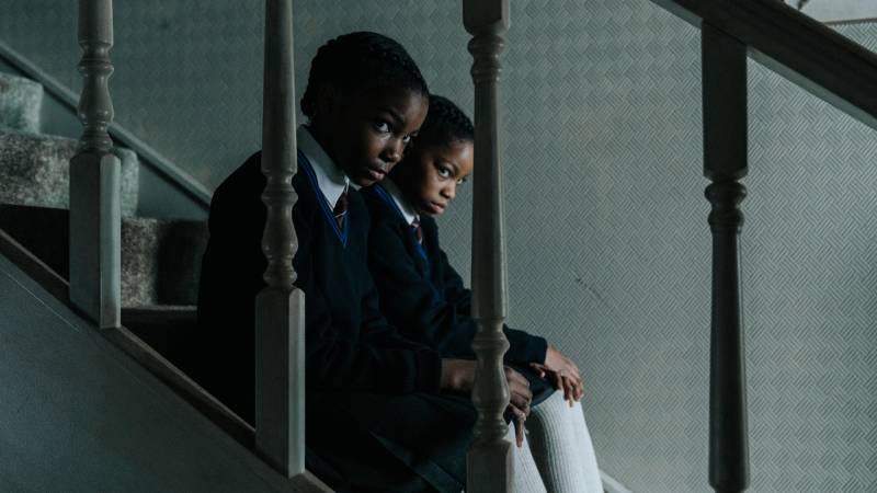 Two young Black girls in school uniforms sit on stairs
