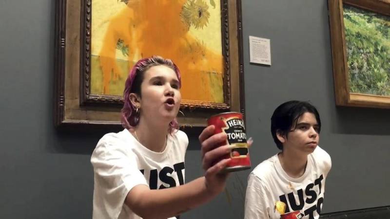 two young activists in white shirts are glued to the wall in front of a defaced painting