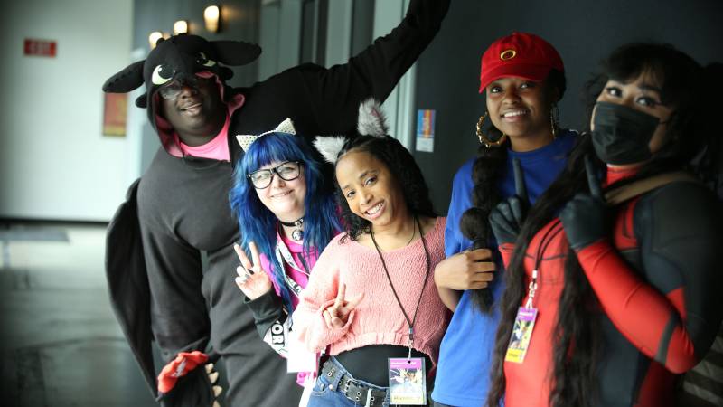 Five people pose and smile at camera in cosplay costumes