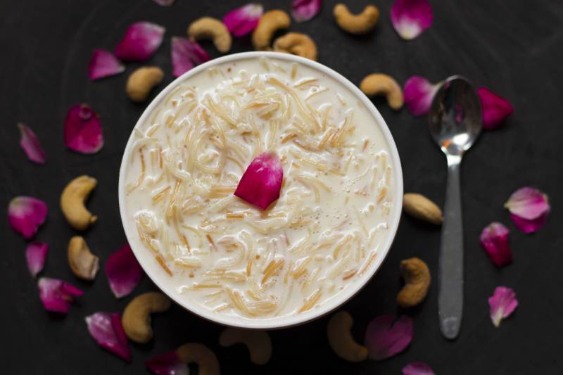 A bowl of rice pudding viewed from above, surrounded by scattered petals.