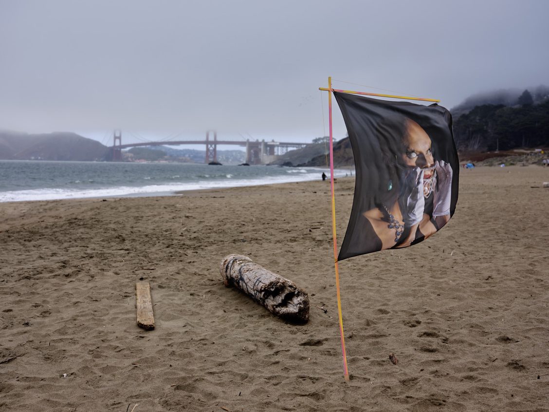 Flag on beach with image of drag performer, Golden Gate Bridge behind