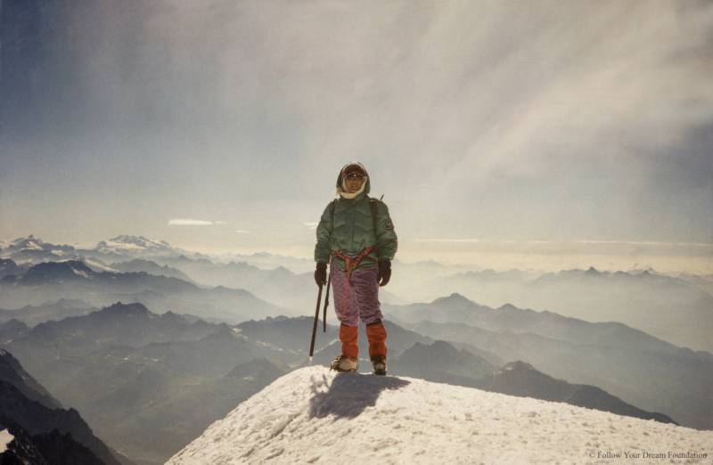 a woman dressed warmly stands atop a mountain