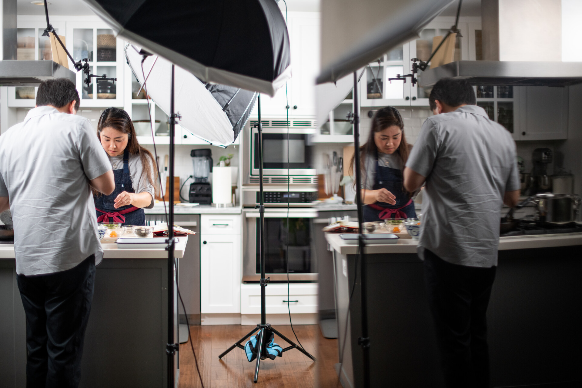 A woman preps food in the kitchen while a man photographs what she's doing; there's a double exposure of this image.
