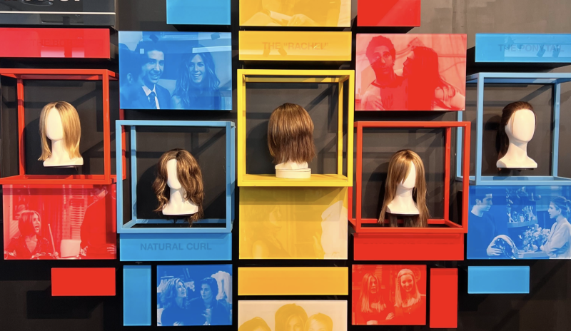 A red, blue and yellow display featuring five dummy heads wearing wigs of different hairstyles.