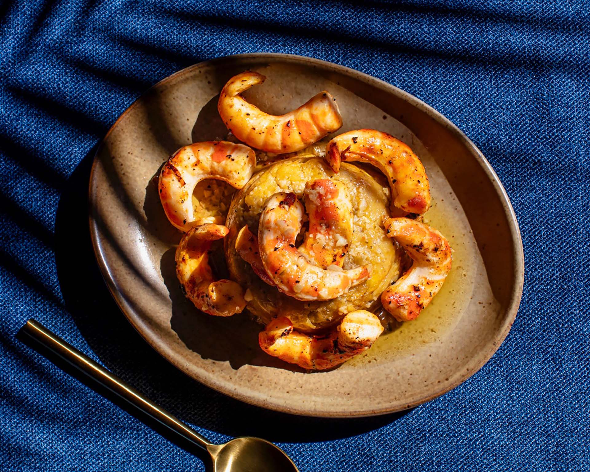 A plate of shrimp mofongo against a dark blue backdrop.