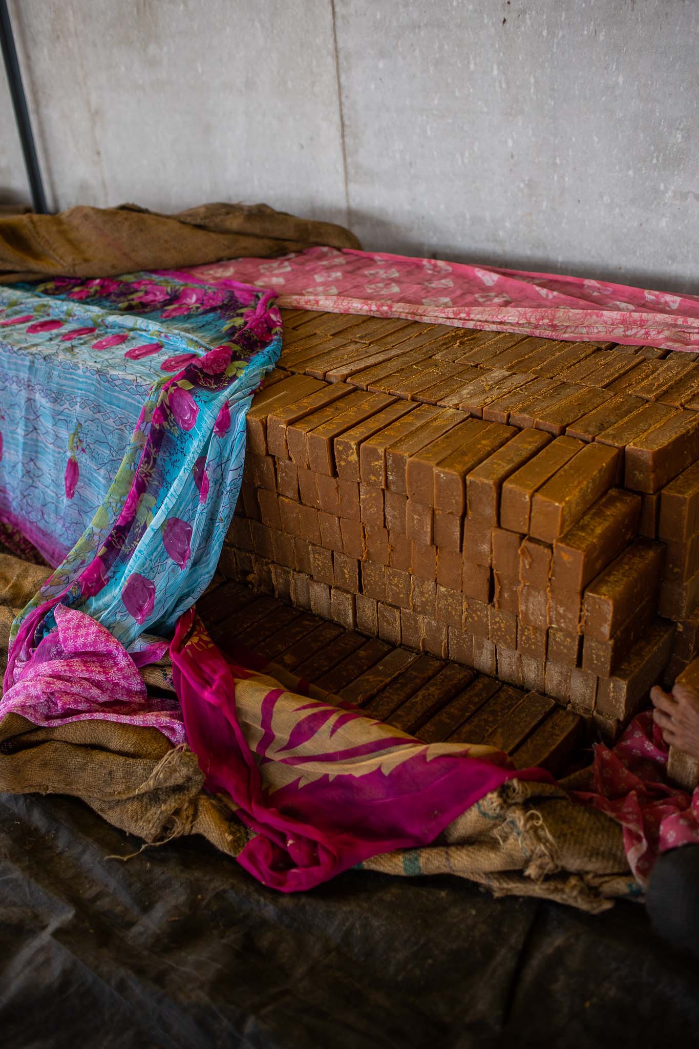 Blocks of jaggery stacked on the ground, draped with colorful cloth.