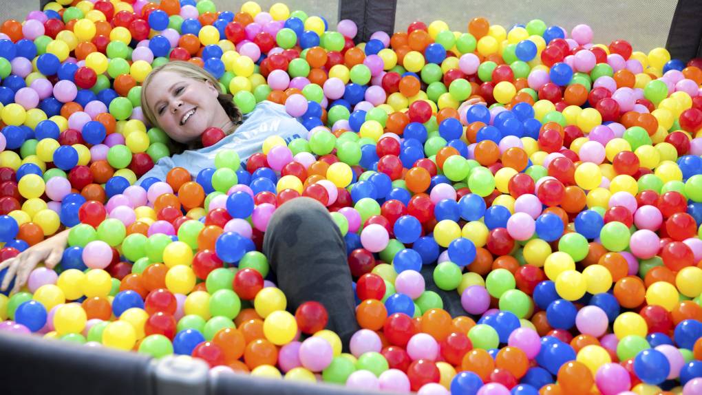 A smiling woman rolls around in a children's ball pit.