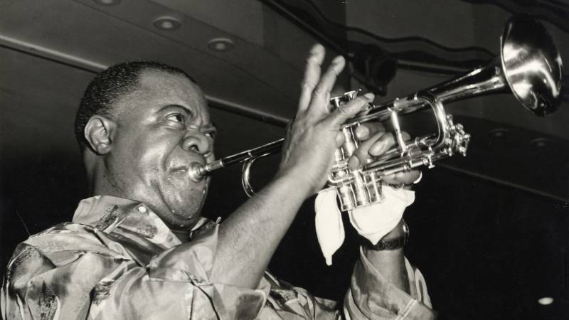 A Black man deep in concentration while playing the trumpet on stage.