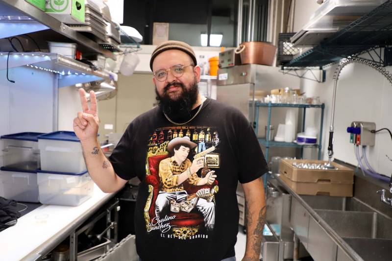 Chef Eder Ramirez stands in the kitchen while giving a peace sign