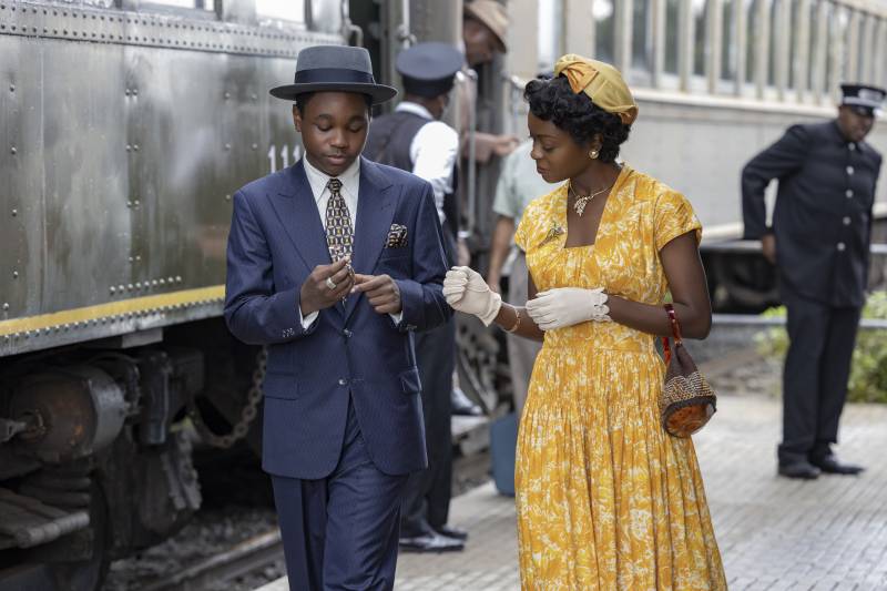 Young Black man in blue suit at train station with Black woman in yellow dress