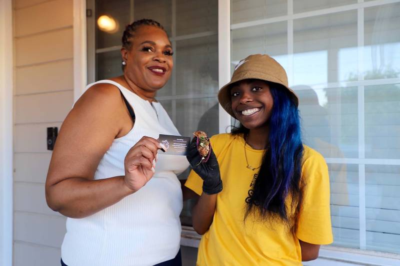 Brea Gladney and her mother both stand in front of their home in San Leandro, while Brea holds one of her vegan fried chicken waffle tacos
