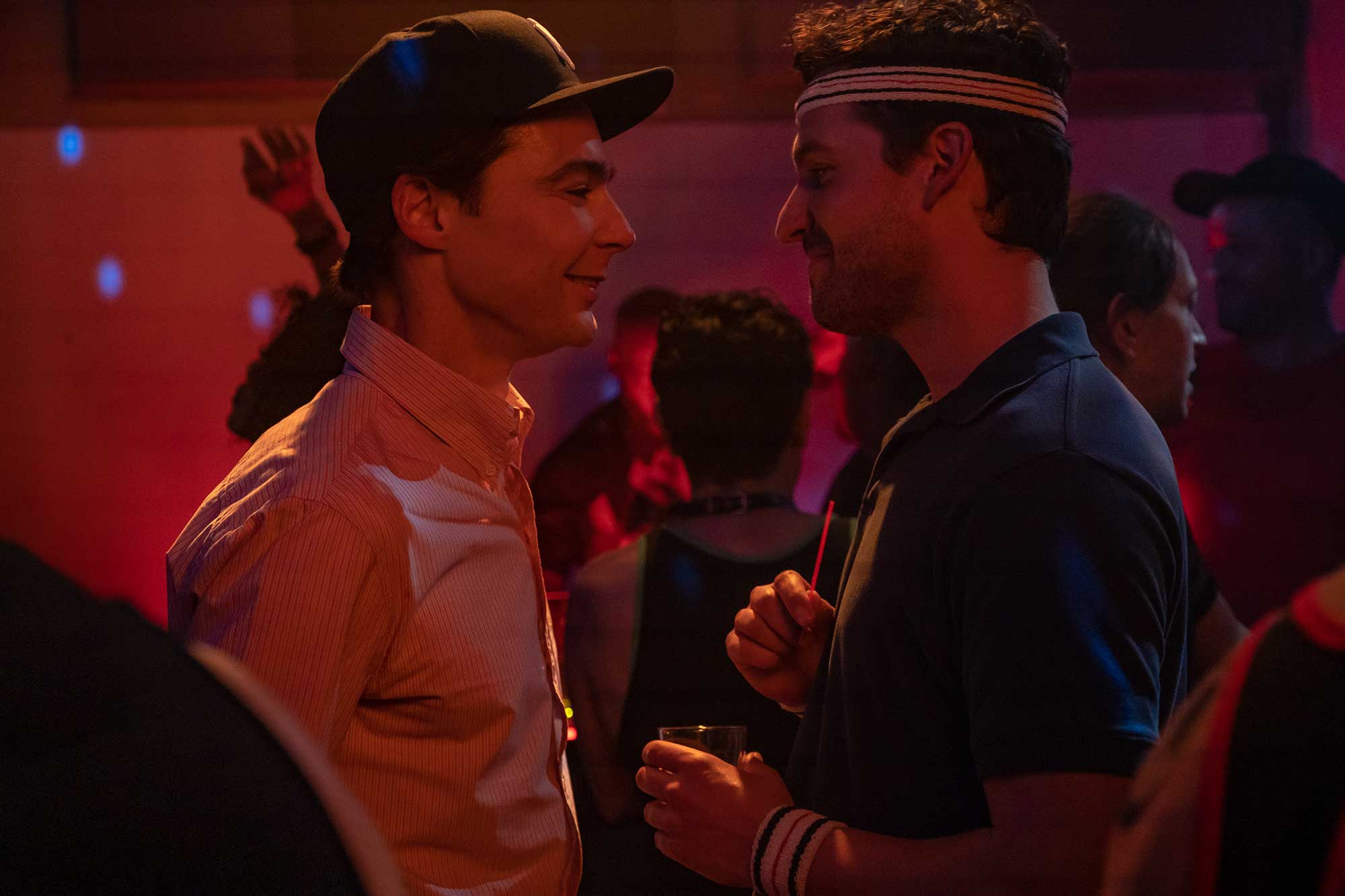 Two white men stand close and smile at each other in pink lit dance scene