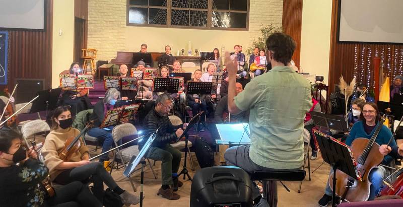 A room of symphonic musicians plays with music stands and instruments