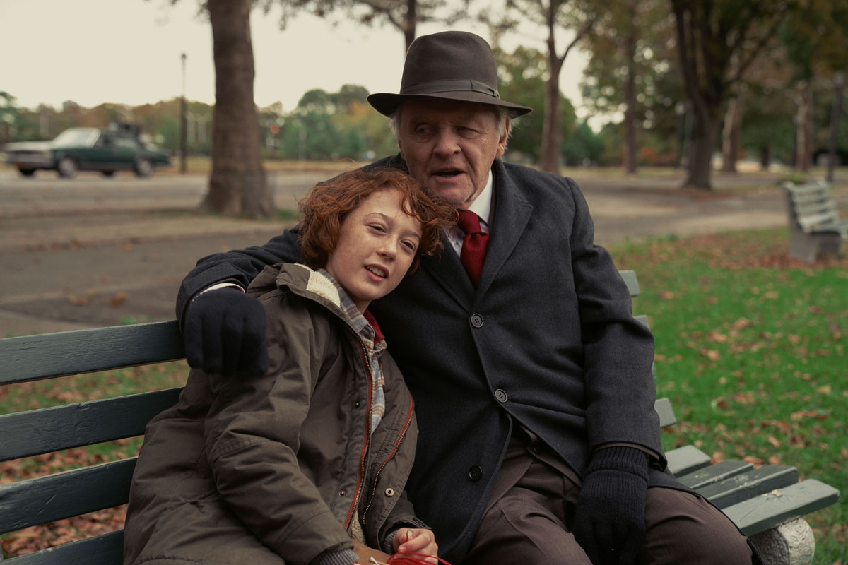 A red-headed white boy and an older white man hug on a park bench