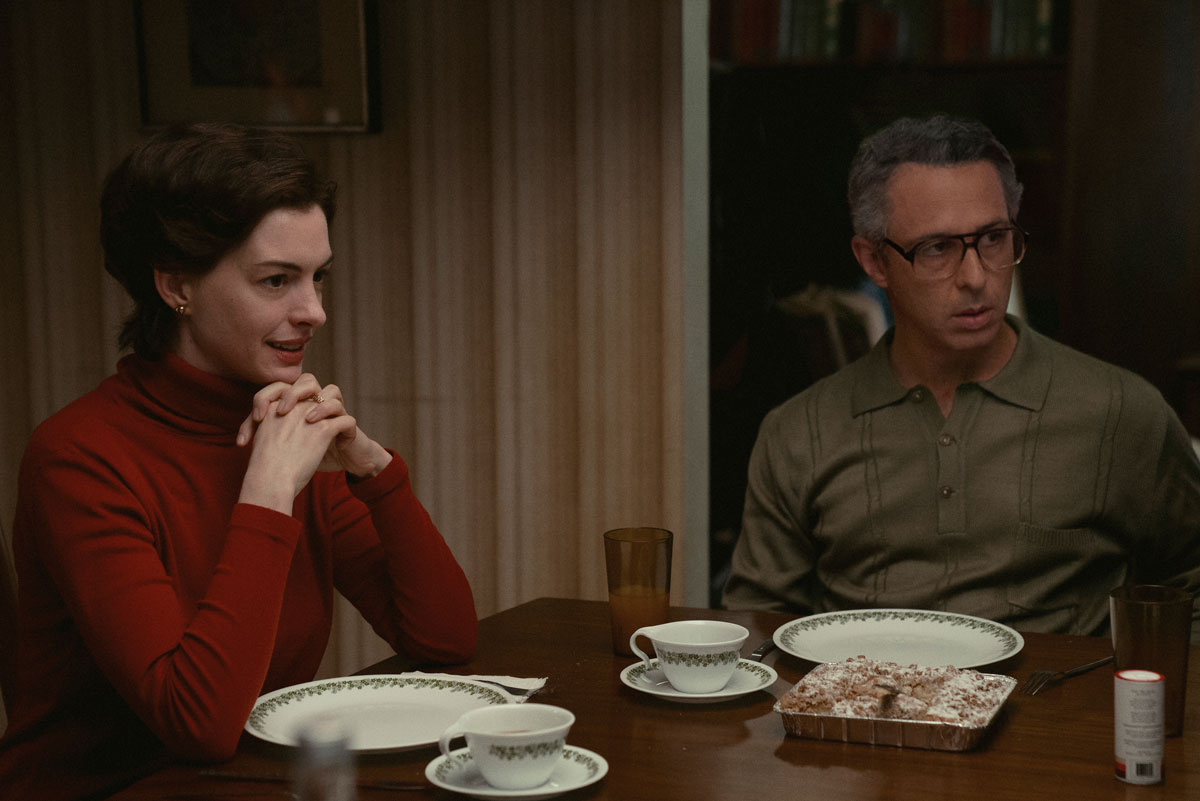 A white woman and a white man sit at dining table with empty plates and pastry